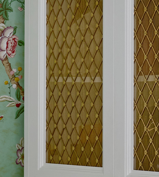 White cabinet front frames inset with best woven metal decorative grilles in basketweave pattern with mesh backing.