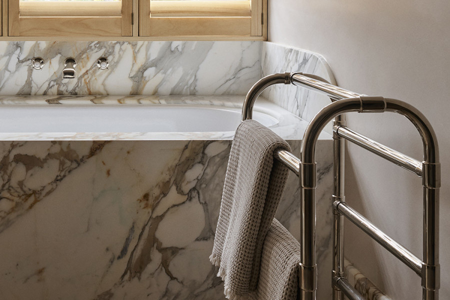 A traditional towel rack next to a marble bath featuring Perrin & Rowe traditional hot and cold taps from In Residence.