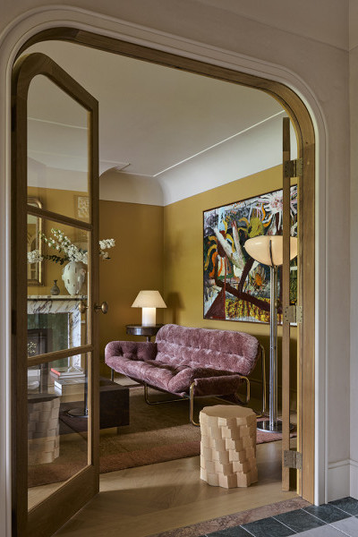 Timber arched doors lead into a yellow living room, with Joseph Giles intricate hammered brass oval doorknobs.
