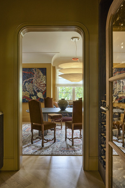 A door with a Joseph Giles hammered brass oval doorknob opens into a wine cupboard and a yellow dining room beyond. 