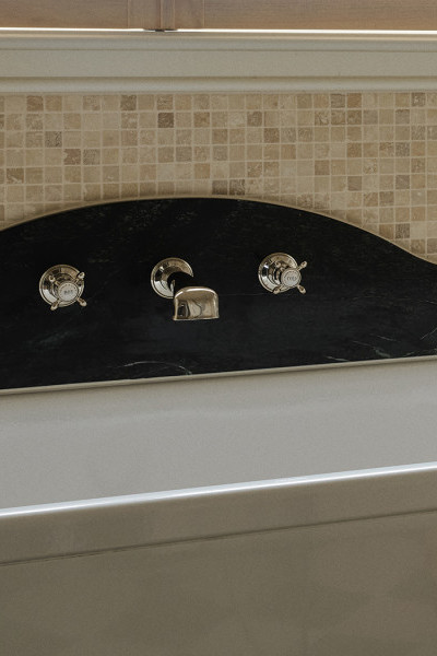 A white bath and green marble backsplash with Perrin & Rowe polished nickel wall-mounted traditional tapware.