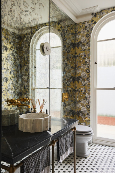 Powder room featuring polished brass tapware, grey Rockwell toilet pan, black marble vanity, and champagne floral wallpaper creating a bold yet elegant design